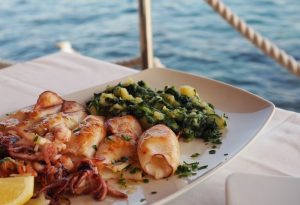 photo of food on a plate with greens a fish in the middle in the background of the photo you can sea the Adriatic sea 